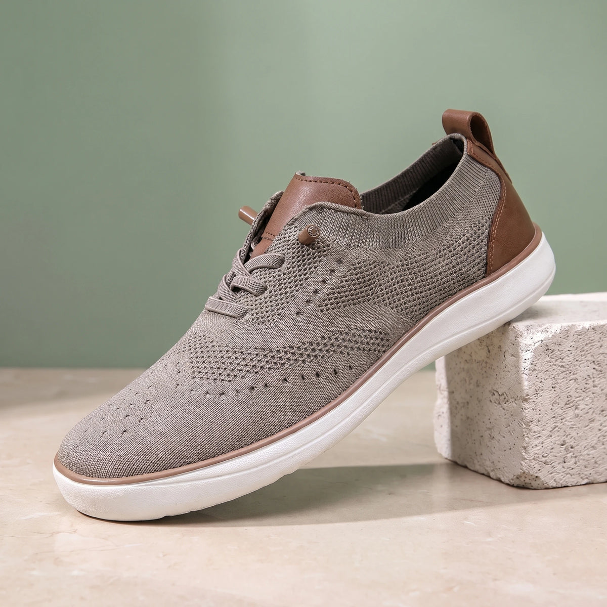 Beige knit lace-up shoe with a white sole on a limestone block